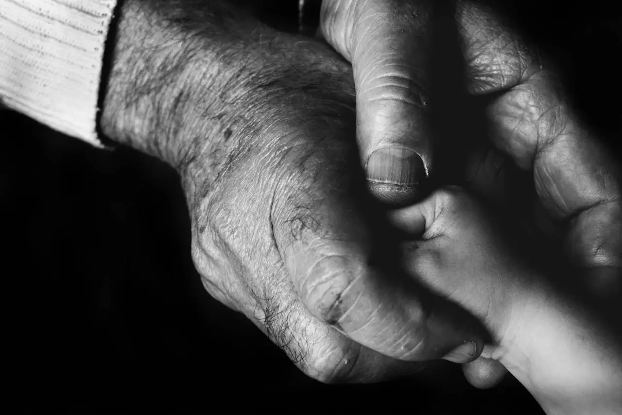 Close-up of elder and childs hands in black and white, symbolizing love and connection.
